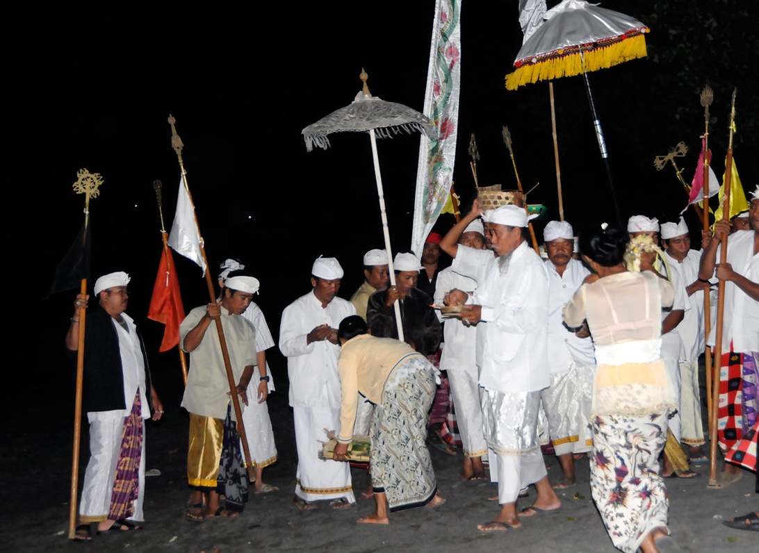 En nattlig traditionell procession där deltagare i vita traditionella kläder bär ceremoniella föremål.
